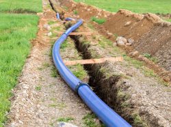 A blue water pipe being installed into the ground.